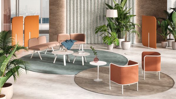 Un moderno ambiente lounge o area d'attesa, caratterizzato da un design accogliente e funzionale, con arredi in linea con le proposte contract di Gaber. Sono presenti diverse sedute imbottite di colore rosa antico e arancione terracotta, disposte attorno a tavolini rotondi bianchi. L'ambiente è definito da due tappeti circolari di diverse tonalità di verde e grigio. Sullo sfondo, grandi piante verdi in vaso aggiungono un tocco naturale. Pannelli divisori arancioni verticali contribuiscono a delineare gli spazi. Le pareti presentano un mix di finiture lisce e a righe verticali. L'immagine suggerisce un ambiente confortevole e stilisticamente curato, ideale per aree comuni in contesti professionali o hospitality.