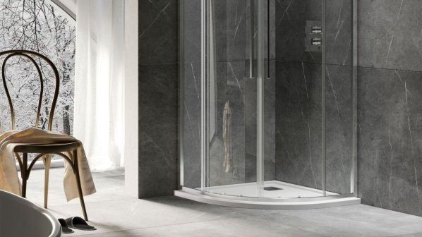 Un elegante bagno moderno con una cabina doccia ad angolo arrotondata del brand Relax, con pareti in vetro trasparente e profili sottili in metallo cromato. La doccia ha un piatto doccia bianco e ante scorrevoli con maniglie verticali. All'interno, un miscelatore a incasso è visibile sulla parete. Le pareti del bagno sono rivestite con piastrelle di grande formato in marmo scuro con venature chiare, che continuano anche sul pavimento. A sinistra, si intravede una vasca da bagno bianca e una sedia in legno curvato con un asciugamano drappeggiato. Una grande finestra ad arco con vista su un paesaggio innevato è visibile sulla sinistra, completando l'atmosfera luminosa e raffinata dell'ambiente.