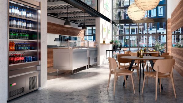 Un ambiente di ristorazione self-service caratterizzato da elementi della linea Basic Lux di Art Serf. In primo piano a sinistra, un espositore refrigerato verticale aperto, di colore grigio metallizzato, pieno di bottiglie e lattine di bevande. Sullo sfondo, un bancone self-service in acciaio inossidabile con teche espositive per alimenti. L'ambiente è definito da grandi finestre che si affacciano sull'esterno, pareti con rivestimenti in legno e cemento, e un pavimento in cemento lucidato. Tre grandi lampade a sospensione sferiche in carta di riso illuminano la zona tavoli, arredata con tavoli rotondi e sedie in legno chiaro. L'immagine enfatizza la funzionalità e il design contemporaneo delle soluzioni self-service di Art Serf per ambienti ampi e luminosi.