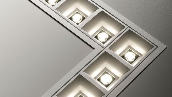 Un apparecchio di illuminazione a incasso del brand Esse-Ci, caratterizzato da un design moderno e pulito. L'illuminatore è composto da una serie di moduli quadrati allineati a formare un angolo retto, incassati in un soffitto o parete di colore chiaro. Ogni modulo contiene una sorgente luminosa circolare che emette una luce bianca brillante. L'immagine, ripresa in un ambiente illuminato, enfatizza la luminosità, l'integrazione architetturale e il design minimale dei prodotti di illuminazione di Esse-Ci.
