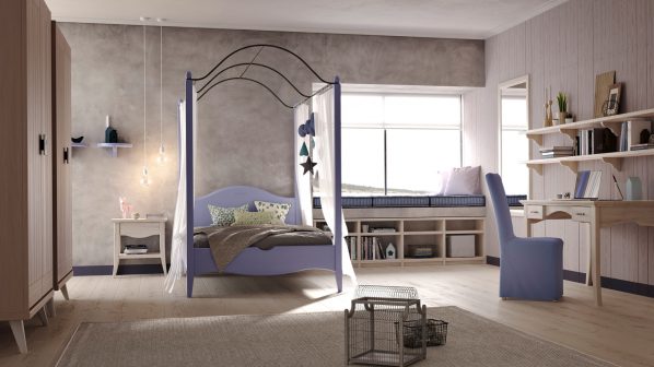 Una spaziosa e luminosa camera per bambini del brand Scandola, caratterizzata da un letto a baldacchino viola chiaro al centro, adornato con tende trasparenti bianche e un piumone grigio. Accanto al letto, sulla sinistra, un comodino bianco con una lampada da tavolo e tre lampadine pendenti con fili lunghi. Sulla parete sinistra, una texture grigia e due mensole blu a muro con vasi neri e un candelabro. Sulla destra, una zona studio con una scrivania in legno chiaro, una sedia azzurra e mensole a muro decorate con libri e oggetti. La finestra sulla destra ha una seduta imbottita in blu e decorazioni a forma di nuvole e stelle nere e verdi. In primo piano, su un tappeto chiaro, si trovano due gabbie decorative per uccelli. Un armadio alto e stretto di colore rosa cipria è visibile sulla sinistra. L'ambiente è illuminato da luce naturale e artificiale, creando un'atmosfera accogliente e funzionale.