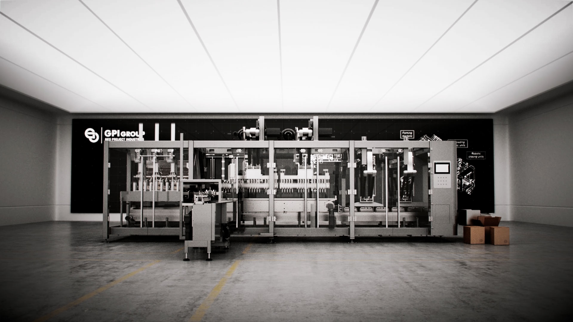 Una fotografia grandangolare mostra un'ampia macchina industriale complessa, composta da moduli in acciaio inossidabile lucido e pannelli trasparenti, posizionata al centro di un grande ambiente rettangolare. Sullo sfondo, una parete scura è decorata con il logo "GPI Group" e "GPI PROJECT INDUSTRY", accompagnato da disegni tecnici e schemi. Il soffitto è illuminato da una serie di pannelli luminosi rettangolari, mentre il pavimento in cemento ha delle linee gialle che delimitano un'area. A destra della macchina, si trovano alcune scatole di cartone impilate. L'immagine trasmette un'atmosfera di efficienza e tecnologia industriale.
