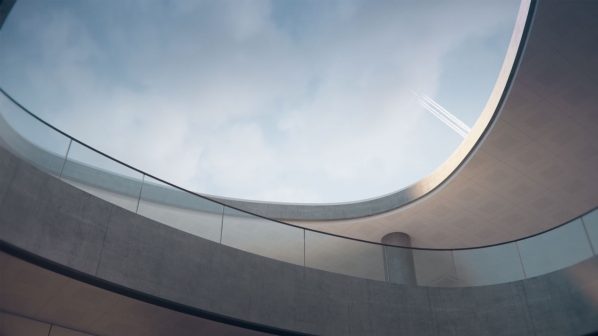 Una vista dal basso verso l'alto di un imponente atrio moderno all'interno di un aeroporto, caratterizzato da ampie strutture curve in cemento a vista e ringhiere in vetro con corrimano sottili. Queste strutture creano aperture circolari e ovali che lasciano intravedere il cielo nuvoloso sopra. La luce naturale inonda lo spazio, creando giochi di ombre sulle superfici curve. L'architettura minimalista e spaziosa è tipica dei terminal aeroportuali contemporanei.