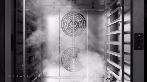Una vista interna in bianco e nero di un forno industriale, riempito di vapore. Al centro della camera di cottura, due grandi ventole circolari sono visibili, circondate da un'atmosfera densa di nebbia. A destra, si vedono i supporti per le teglie, mentre il lato sinistro include parte della porta del forno. In basso a sinistra, la parola "METAVERSO" è visibile. L'illuminazione dall'alto crea riflessi metallici sulle superfici interne.
