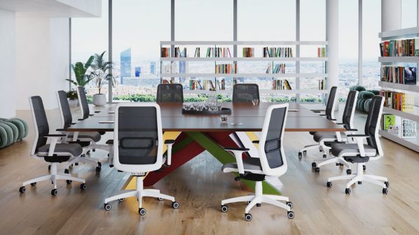 Una grande e moderna sala riunioni o ufficio con finestre dal pavimento al soffitto che si affacciano su uno skyline urbano. Al centro della stanza, un lungo tavolo ovale in legno scuro è circondato da dieci sedie da ufficio girevoli con schienale in rete nera e sedili imbottiti grigi. Le basi e i braccioli delle sedie sono bianchi. Le gambe del tavolo sono di un vivace mix di colori rossi, verdi e gialli. Sulla destra, una libreria bianca a giorno con libri colorati, e a sinistra una grande pianta in vaso.