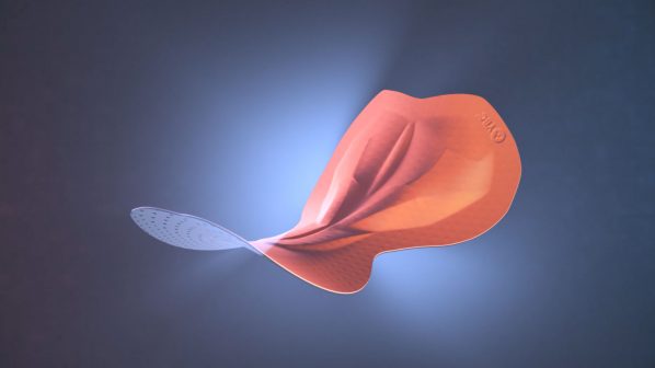 Un cuscinetto da ciclismo di colore arancione bruciato con una superficie ondulata e tridimensionale, che sfuma in un'area traforata bianca e trasparente sulla sinistra. Il cuscinetto è sospeso su uno sfondo scuro e sfumato di blu e grigio, con un punto di luce brillante al centro. Una piccola etichetta rotonda con del testo è visibile in alto a destra.