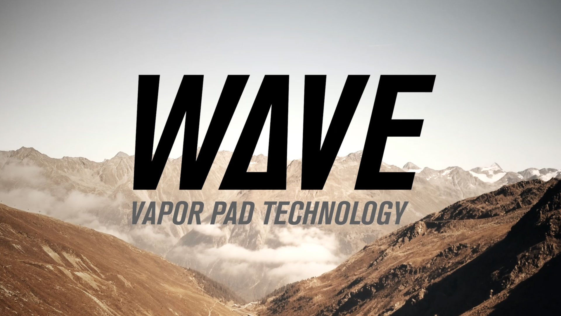 Un logo grande e in grassetto con la parola "WAVE" in nero, con la "A" stilizzata come un'onda o una "V" con una linea diagonale che la attraversa. Sotto, in un carattere più piccolo e grigio, la scritta "VAPOR PAD TECHNOLOGY". Lo sfondo è un paesaggio montano nebbioso, con cime rocciose e valli coperte da nuvole o foschia, illuminato dalla luce del sole.
